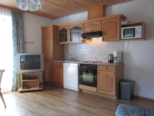 cocina con armarios de madera, fogones y TV en Appartement Grubbauer, en Wagrain
