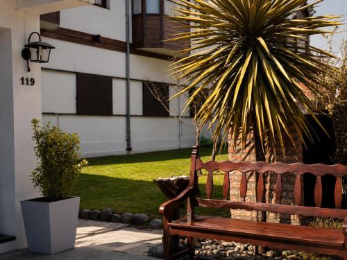 a wooden bench in front of a house with a palm tree at Kalken Hotel by MH in El Calafate