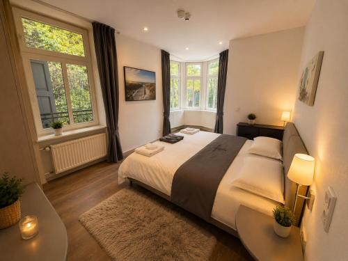 a bedroom with a large bed with two tables and two windows at Kurvilla Hotel & Apartment in Landstuhl