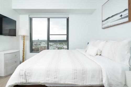 a white bedroom with a large bed and a window at Central Upscale 2BR Condo wGym Office & Parking in Cambridge