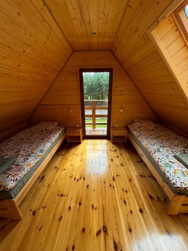 two beds in a wooden room with a window at Mazurski lasek in Szwejkowo