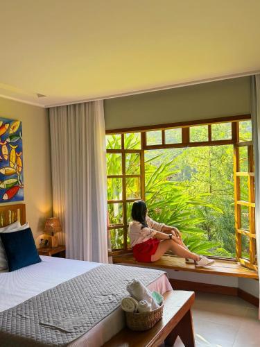 a woman sitting on a window sill in a bedroom at Pousada e Restaurante Vila do Loro in Domingos Martins