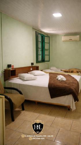 a bedroom with two beds and a chair at Hotel São Luiz Iraí in Iraí