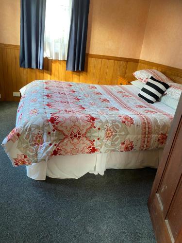 a bedroom with a bed with a red and white quilt at Waitomo Farmstay - Rimu Cottage 2 in Waitomo Caves