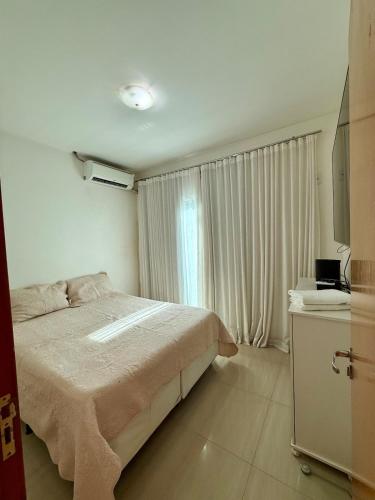 a white bedroom with a bed and a window at Sobrado Flamboyant in Goiânia