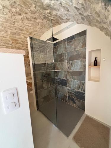 a glass shower in a bathroom with a stone wall at Maison éla in Bessas