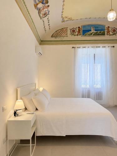 a white bedroom with a bed and a window at Liolà Rooms in Terrasini