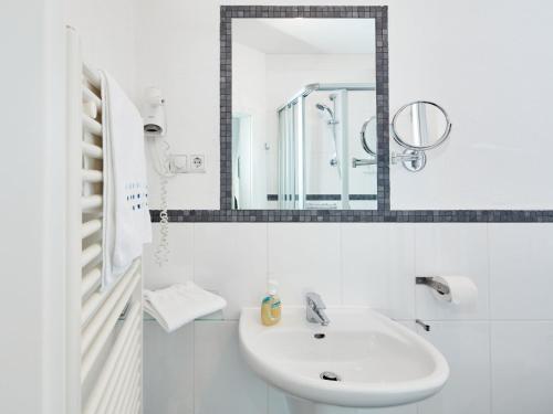 a white bathroom with a sink and a mirror at Püttmanns Dorfhotel in Olpe