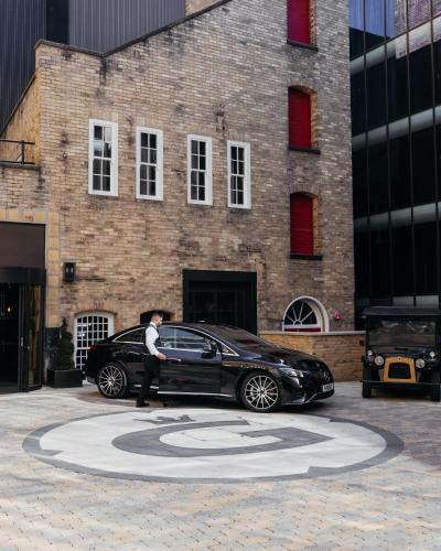 a man walking past a black car in front of a building at Hotel Gotham Newcastle in Newcastle upon Tyne