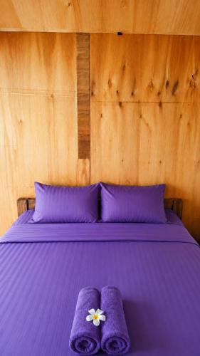 a purple bed with purple pillows and two purple towels at Garden Cottage in Gili Gede
