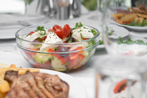 a salad in a bowl on a table with a plate of food at Cosmopolitan Hotel in Paralia Katerinis