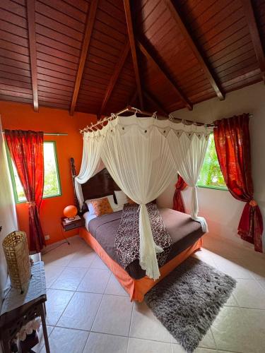 a bedroom with a canopy bed with red curtains at Gite d'Arles Bungalow "Orchidée" in Le Moule
