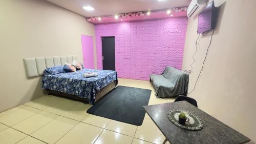 a room with a bed and a table and a purple wall at Quarto próximo ao parque de exposição BR163 in Dourados