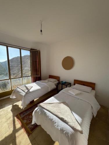 two beds in a room with a large window at Dana Village lodge and Camp-Wadi Dana Eco camp in Dana