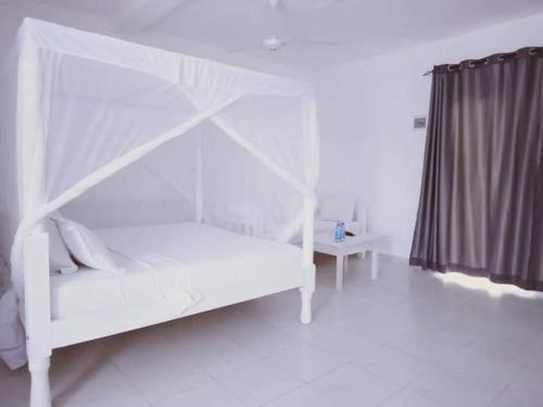 a white bedroom with a white bed and a table at Butah Gardens Watamu in Gede