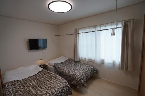 a bedroom with two beds and a television and a window at エル白馬 L hakuba in Hakuba