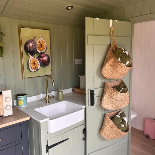 a kitchen with a sink and baskets on the wall at Shepherds Hut in Shropshire with Swimming Pool in Shifnal