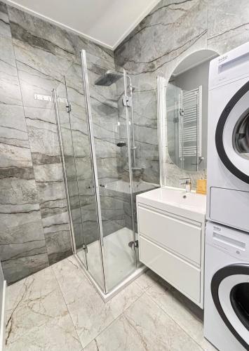 a bathroom with a shower and a sink and a washing machine at Marigold Apartment Łódź in Łódź