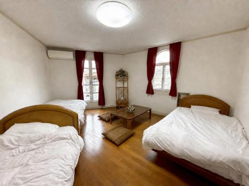 a bedroom with two beds and a table and two windows at ホワイトホテル鎌倉 in Kamakura