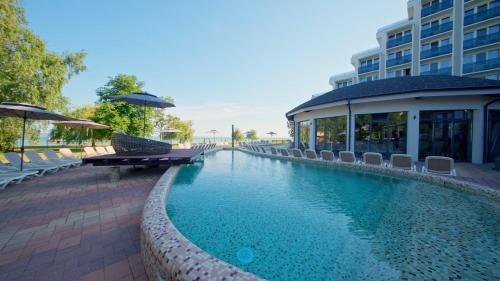 a swimming pool with chairs and umbrellas next to a building at Premium Hotel Panoráma in Siófok