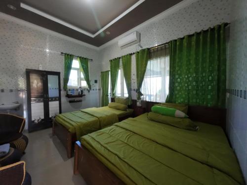 two beds in a bedroom with green curtains at Fathin Hotel Bawean Syariah in Sangkapura