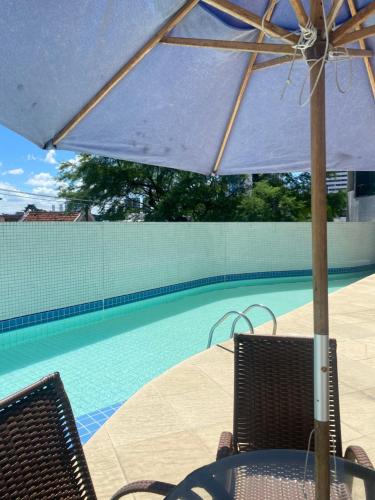 a table and chairs with an umbrella next to a swimming pool at Apto com localização privilegiada e piscina - Charmoso e completo in Recife