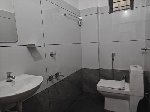 a white bathroom with a sink and a toilet at Uthram Avenue in Tāmarakulam