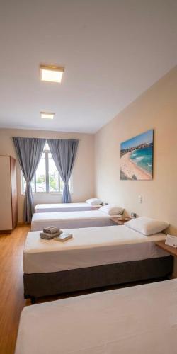 a hotel room with three beds and a window at Vintagyn Hostel in Goiânia