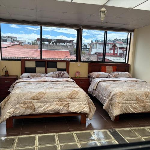 two beds in a room with large windows at Hostal Mediodía MATRIZ in Quito