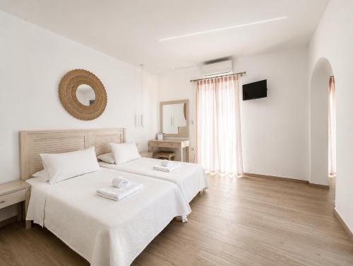 a white bedroom with two beds and a mirror at Cyclades Blue in Ornos