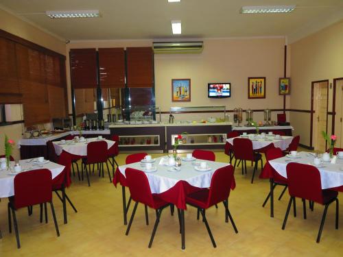 a restaurant with white tables and red chairs and a kitchen at Hotel Castelo Branco in Chimoio