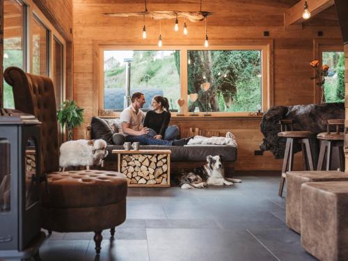 ein Paar sitzt mit zwei Hunden auf einer Couch in einem Wohnzimmer in der Unterkunft Romantikchalet Fuchsbau mit eigenen Wellnessbereich, Komfort und viel Ruhe in der Natur in Vorra