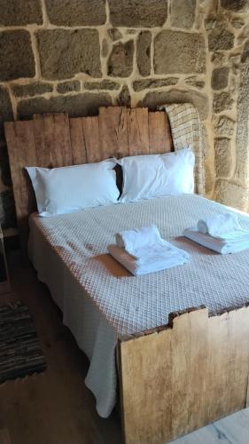 a bed with white sheets and pillows in front of a stone wall at Fuinhas de Amor a 2 in Fuinhas