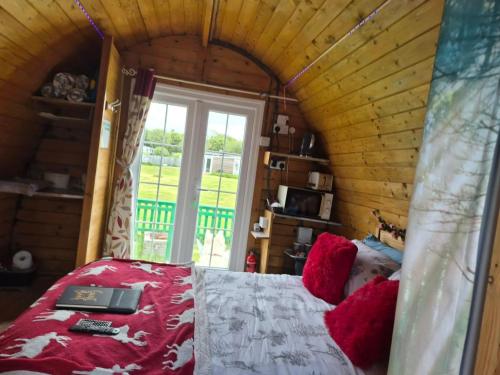 a bedroom with a bed with red pillows and a window at Glamping Pod in St Austell Sleeps 2 with Spa Pool in Lanivet