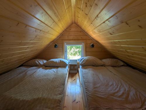two beds in a wooden room with a window at Chill House Sedranki in Olecko