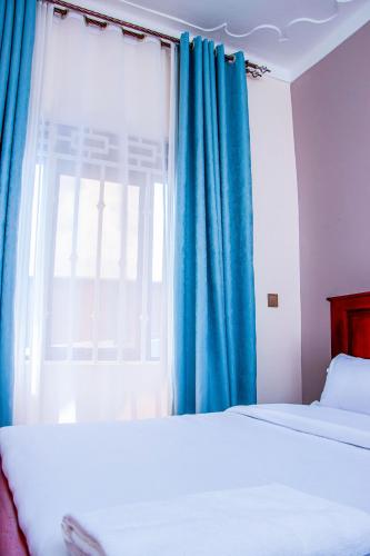 a bedroom with two beds and a window with blue curtains at Gugga Suites Mbale in Mbale