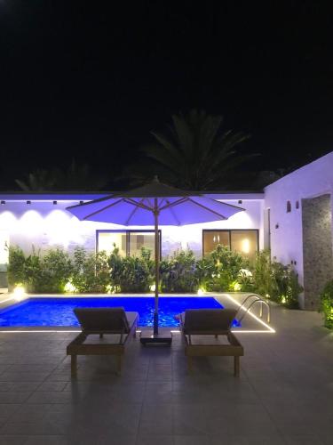 a patio with two chairs and an umbrella at night at شاليهات دبليو العمارية in Al ‘Ammārīyah