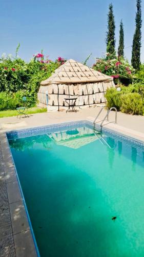 a large swimming pool with a picnic table and a thatched shelter at Villa à Marrakech in Oulad Sidi Cheïkh