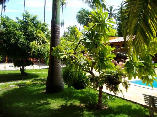 a group of people sitting next to a pool with palm trees at Pousada Recanto do Sossego in Itamaracá