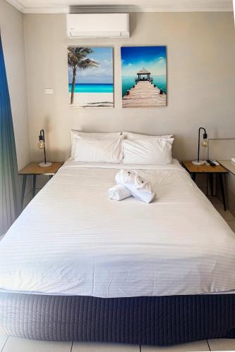 a bedroom with a large white bed with two paintings on the wall at U240 Dhr in Eimeo