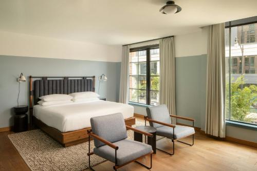 a bedroom with a bed and two chairs and windows at The Junto Hotel in Columbus