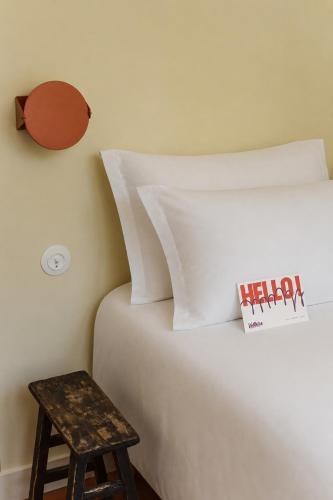 a bed with white sheets and a stool next to it at Hôtel Le Voltaire in Arles