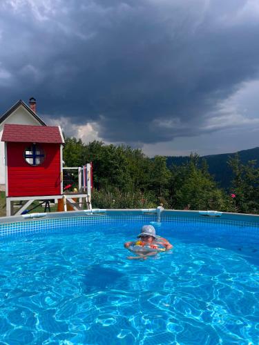 a person in a swimming pool next to a red house at Vila Sekvoja in Nova Varoš