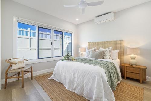 a white bedroom with a bed and a window at Basalt Beach House in Bargara