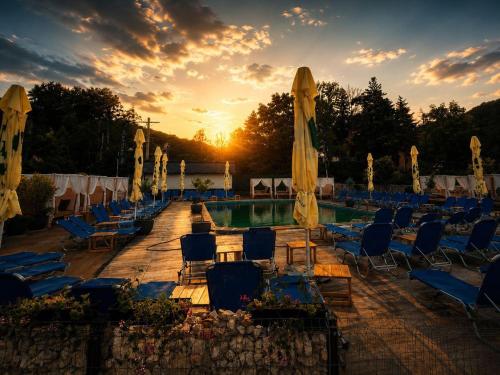 a swimming pool with chairs and umbrellas at sunset at Hotel Sallaris Monteoru in Sărata-Monteoru