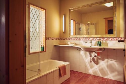 ein Badezimmer mit Badewanne, Waschbecken und Spiegel in der Unterkunft Hotel Hohenfels in Tannheim