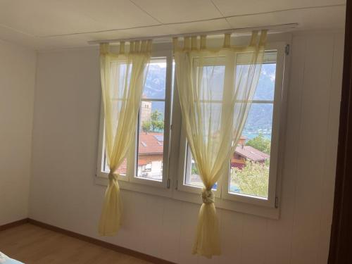 a room with two windows with yellow curtains at Sam's Lakeview apartment in Ringgenberg