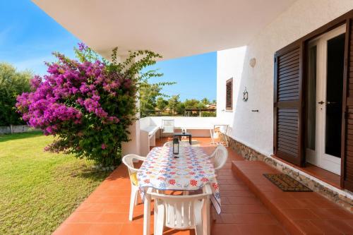 a patio with a table and chairs and a plant with purple flowers at Carasau 200m from the Beach - Garden - BBQ - Wi-Fi - Parking - Pet Friendly in Budoni