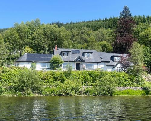a large house on a hill next to a body of water at Ardross Cottage in Aberfoyle