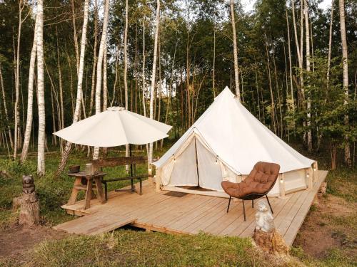 a white tent and a chair on a wooden deck at Glempings Pasaka un pirts I tent and sauna in Vecumnieki